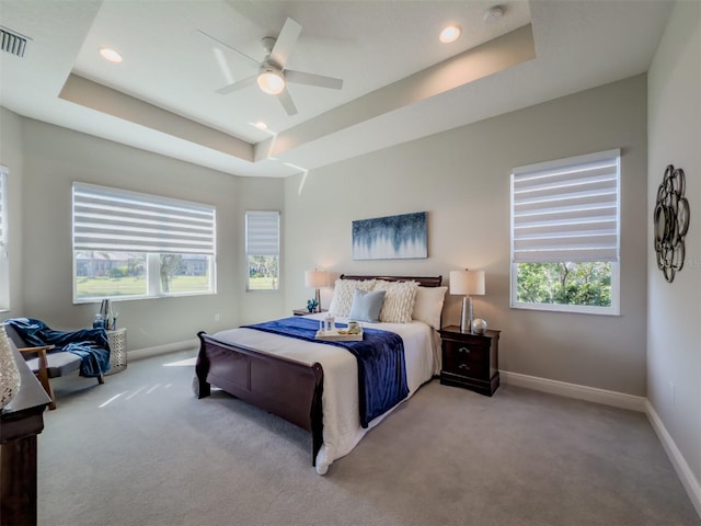 carpeted bedroom with a raised ceiling and ceiling fan