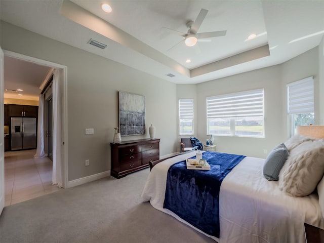 carpeted bedroom featuring ceiling fan, stainless steel fridge with ice dispenser, and a tray ceiling