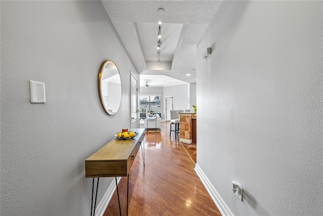 hallway with rail lighting, wood-type flooring, and a textured ceiling