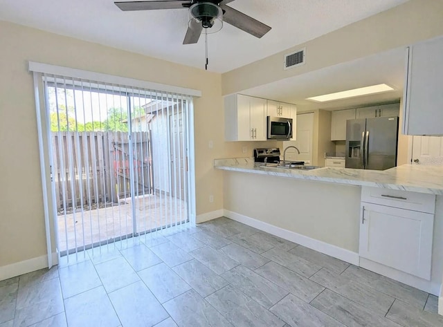 kitchen with kitchen peninsula, ceiling fan, appliances with stainless steel finishes, white cabinetry, and light stone countertops