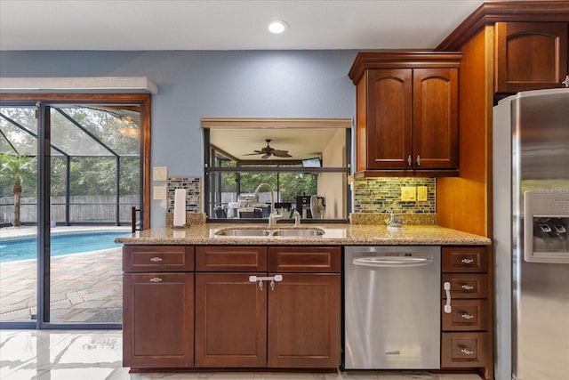 kitchen featuring light stone counters, ceiling fan, appliances with stainless steel finishes, backsplash, and sink