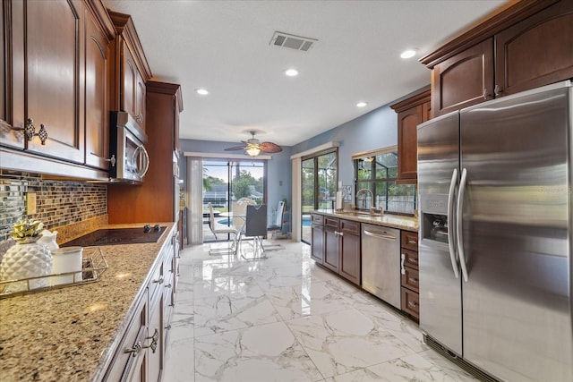 kitchen with ceiling fan, stainless steel appliances, light stone counters, and a wealth of natural light