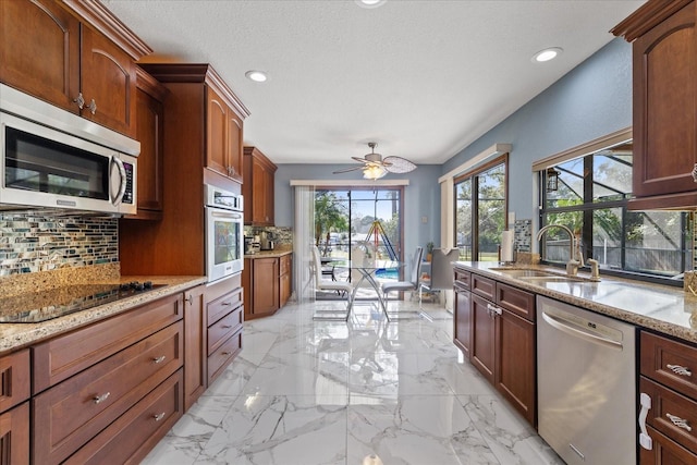 kitchen featuring backsplash, sink, appliances with stainless steel finishes, light stone counters, and ceiling fan