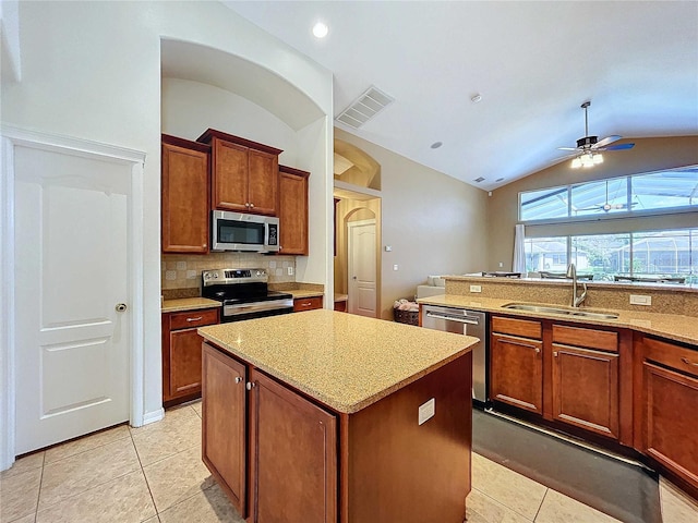 kitchen with light tile patterned floors, appliances with stainless steel finishes, a kitchen island, vaulted ceiling, and sink