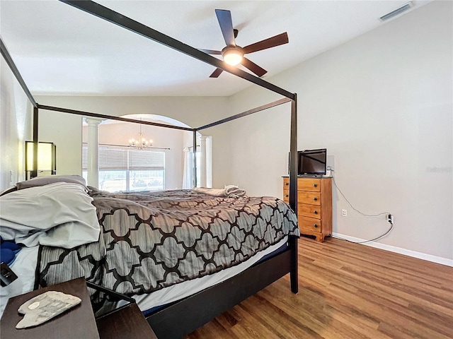 bedroom featuring ornate columns, hardwood / wood-style flooring, ceiling fan with notable chandelier, and vaulted ceiling