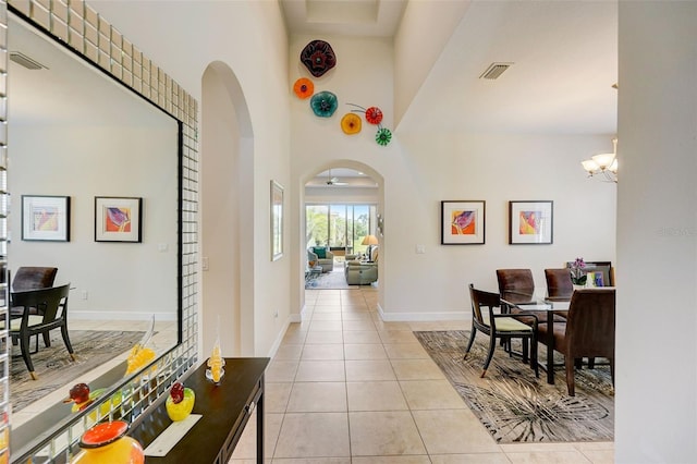 hallway featuring a high ceiling, light tile patterned flooring, and an inviting chandelier