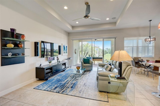 living room with light tile patterned flooring, a tray ceiling, and ceiling fan with notable chandelier