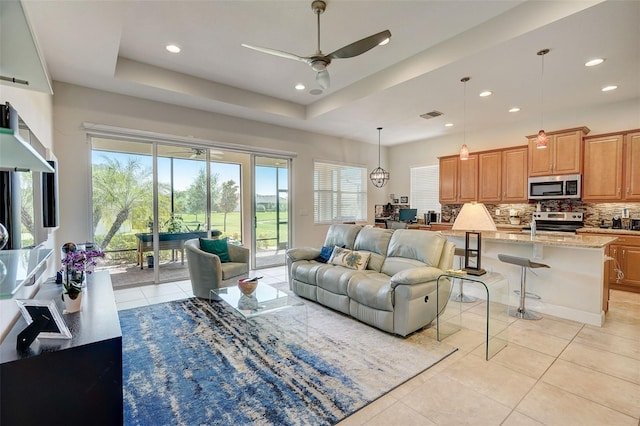 living room featuring ceiling fan, a tray ceiling, and light tile patterned floors