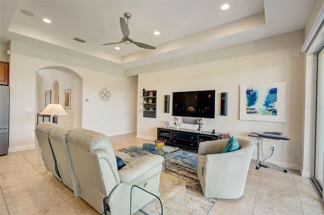 living room featuring ceiling fan, a raised ceiling, and light tile patterned flooring