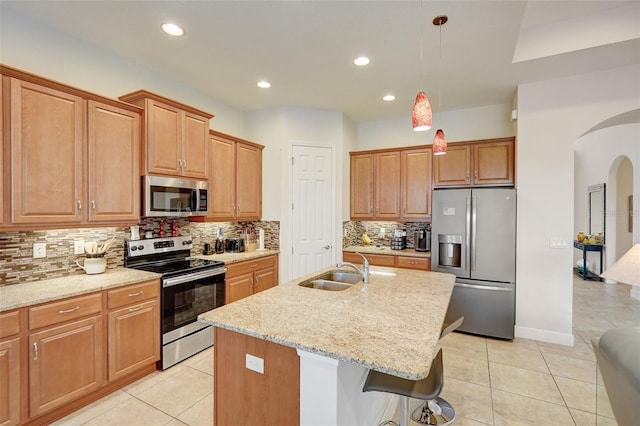 kitchen with an island with sink, a breakfast bar, pendant lighting, appliances with stainless steel finishes, and light stone counters