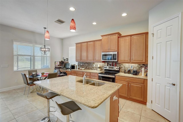 kitchen featuring a center island with sink, hanging light fixtures, light stone countertops, sink, and stainless steel appliances