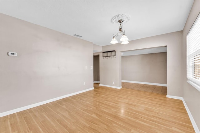 empty room featuring a notable chandelier and light hardwood / wood-style flooring