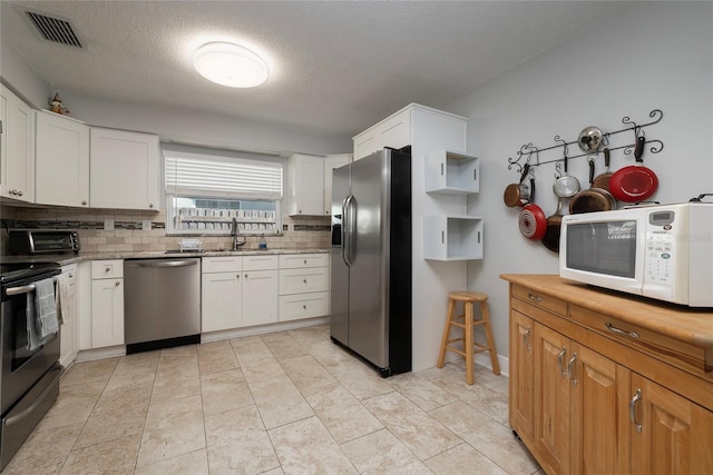 kitchen with sink, appliances with stainless steel finishes, a textured ceiling, backsplash, and white cabinets