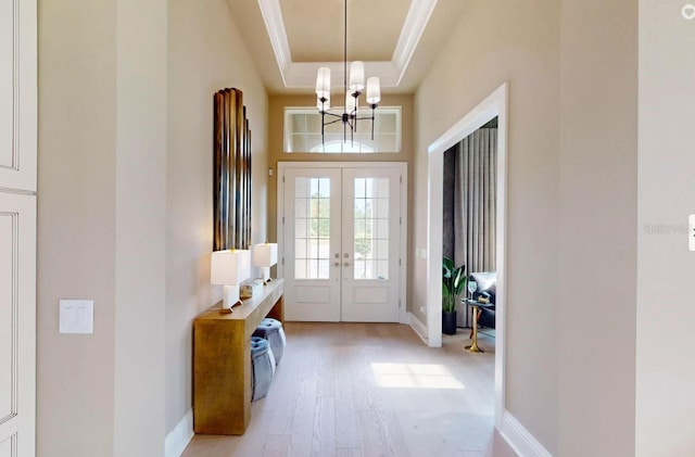 doorway featuring ornamental molding, a notable chandelier, light hardwood / wood-style floors, french doors, and a raised ceiling