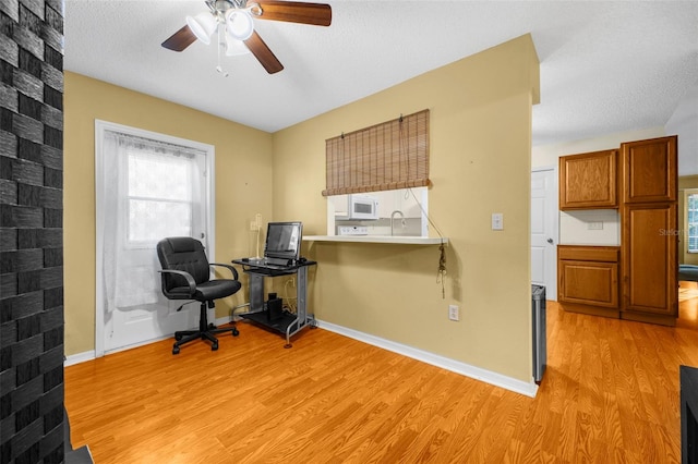 home office with ceiling fan, a textured ceiling, light wood-type flooring, a sink, and baseboards