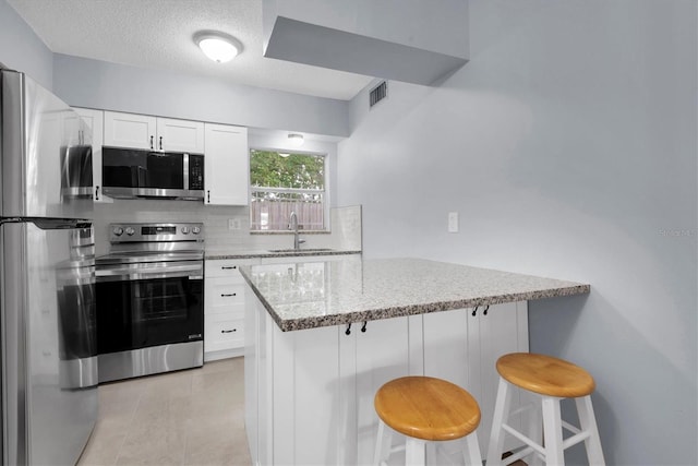 kitchen with kitchen peninsula, a kitchen breakfast bar, white cabinetry, light stone countertops, and stainless steel appliances