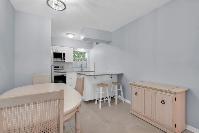 kitchen featuring sink, a textured ceiling, kitchen peninsula, stainless steel appliances, and a breakfast bar