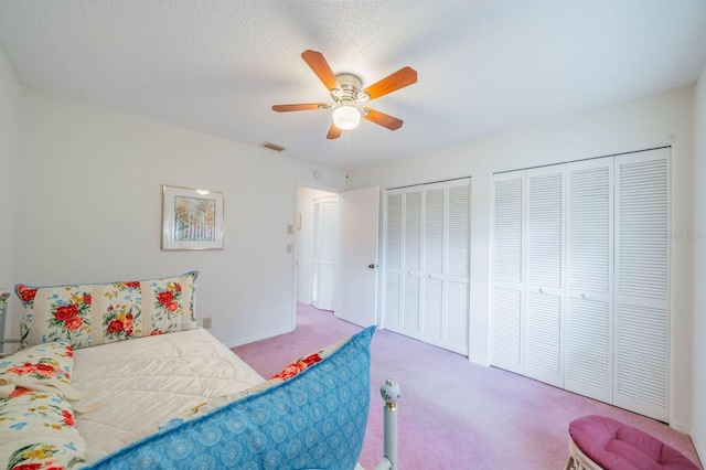 bedroom featuring carpet floors, multiple closets, a textured ceiling, and ceiling fan