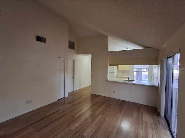 unfurnished living room with high vaulted ceiling, wood-type flooring, sink, and a textured ceiling