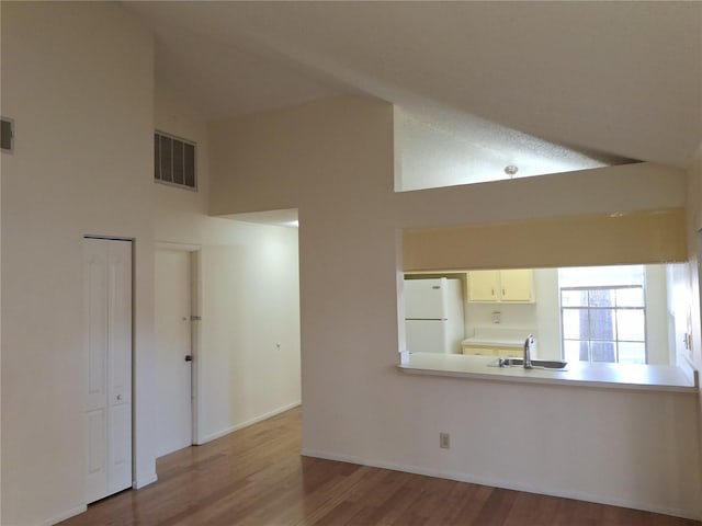 unfurnished living room with sink, light hardwood / wood-style flooring, a textured ceiling, and high vaulted ceiling