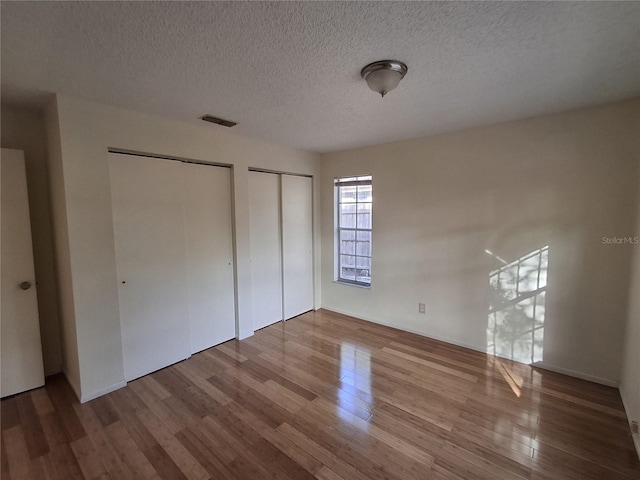 unfurnished bedroom featuring multiple closets, wood-type flooring, and a textured ceiling