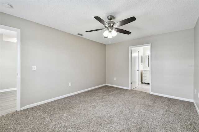 unfurnished bedroom featuring a textured ceiling, light colored carpet, ceiling fan, and ensuite bathroom