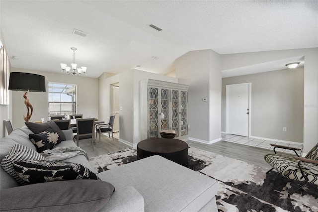 living room featuring light hardwood / wood-style floors, lofted ceiling, a textured ceiling, and a notable chandelier