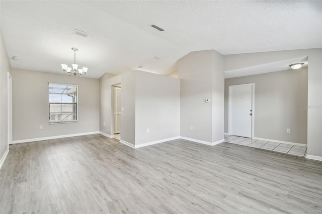 empty room with light wood-type flooring, a notable chandelier, a textured ceiling, and vaulted ceiling