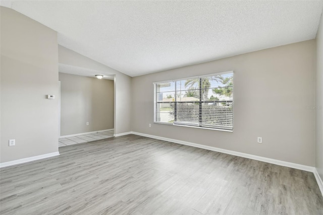 spare room with light wood-type flooring, a textured ceiling, and vaulted ceiling