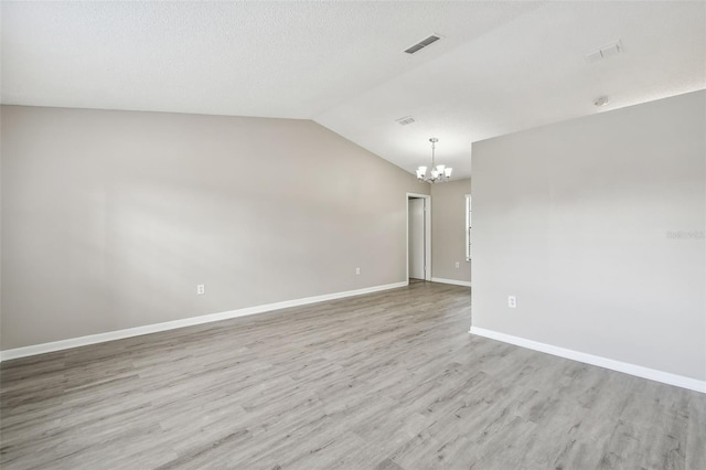 unfurnished room with light wood-type flooring, a notable chandelier, and vaulted ceiling