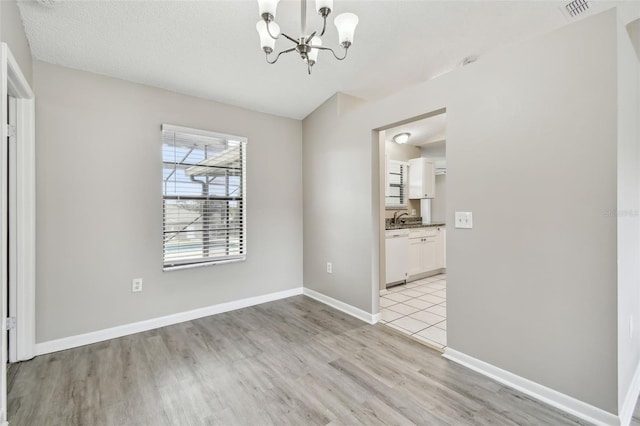 unfurnished dining area with light hardwood / wood-style floors, a notable chandelier, and a textured ceiling