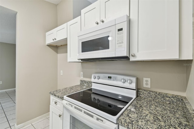 kitchen featuring dark stone counters, white appliances, light tile patterned floors, and white cabinets