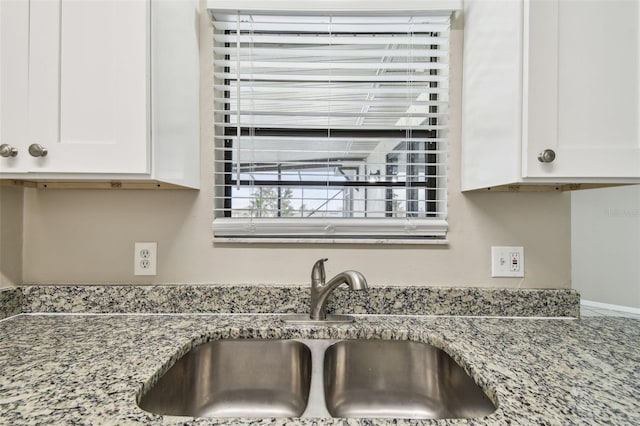 interior details with white cabinets, stone counters, and sink