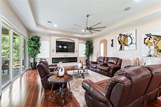 living room with dark hardwood / wood-style floors, ceiling fan, and a tray ceiling