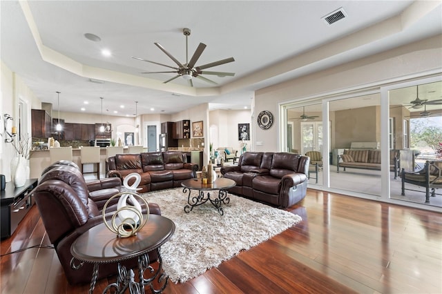 living room with hardwood / wood-style floors, ceiling fan, and a raised ceiling