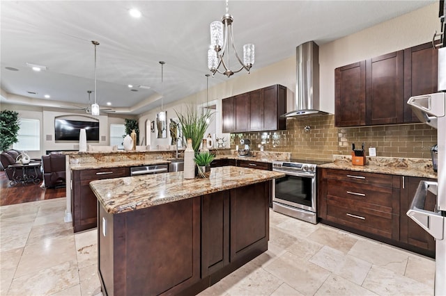 kitchen featuring light stone counters, a kitchen island, wall chimney range hood, appliances with stainless steel finishes, and decorative light fixtures