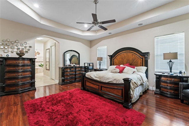 bedroom featuring a tray ceiling, multiple windows, hardwood / wood-style flooring, and ceiling fan