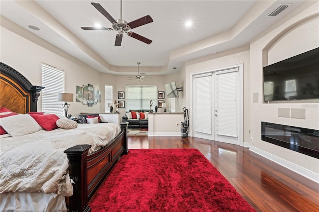 bedroom featuring multiple windows, dark hardwood / wood-style floors, ceiling fan, and a tray ceiling