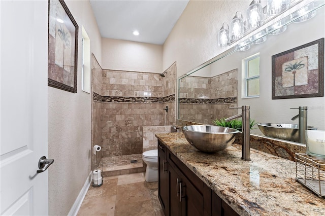 bathroom with a tile shower, vanity, and toilet