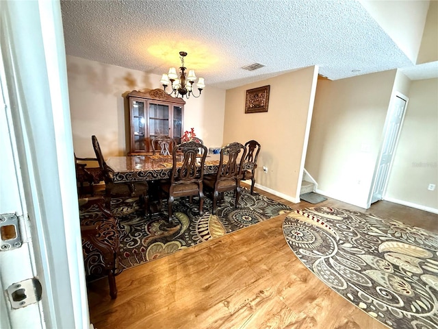 dining space with a chandelier, wood-type flooring, and a textured ceiling