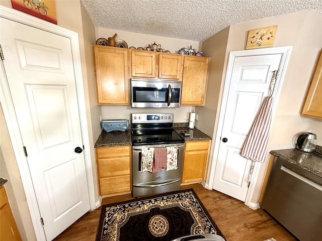 kitchen with appliances with stainless steel finishes, dark stone counters, a textured ceiling, and dark hardwood / wood-style flooring