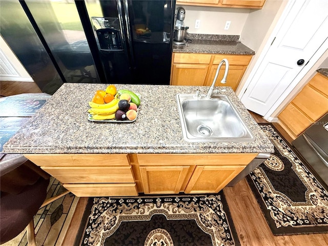 kitchen with light stone counters, sink, hardwood / wood-style floors, and black fridge with ice dispenser