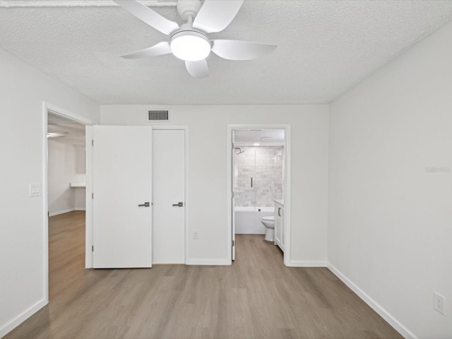 unfurnished bedroom with ceiling fan, connected bathroom, a closet, a textured ceiling, and light hardwood / wood-style flooring