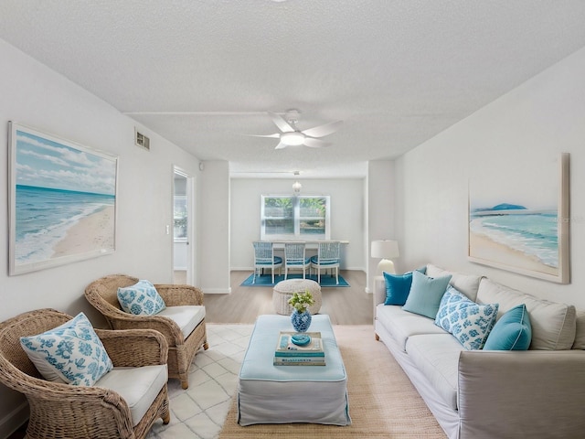 living room featuring ceiling fan, light wood-type flooring, and a textured ceiling