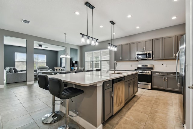 kitchen with stainless steel appliances, a breakfast bar, ceiling fan with notable chandelier, decorative light fixtures, and an island with sink