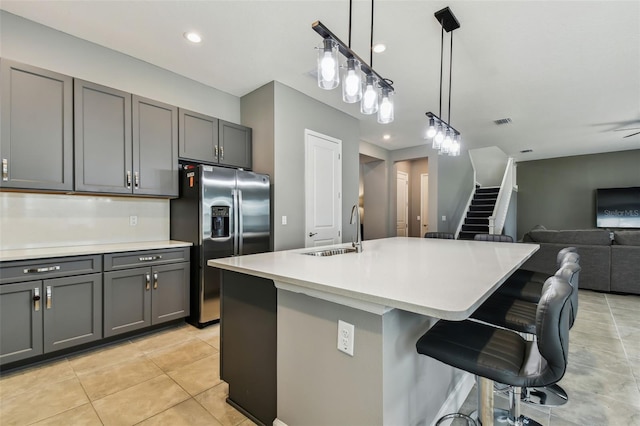 kitchen featuring stainless steel refrigerator with ice dispenser, gray cabinets, a center island with sink, and a breakfast bar