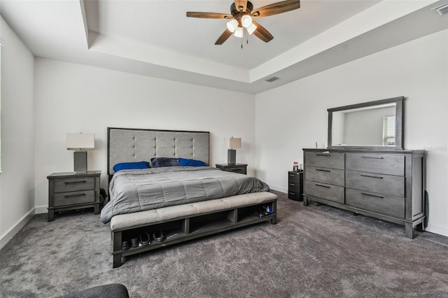 bedroom with ceiling fan, a tray ceiling, and dark carpet