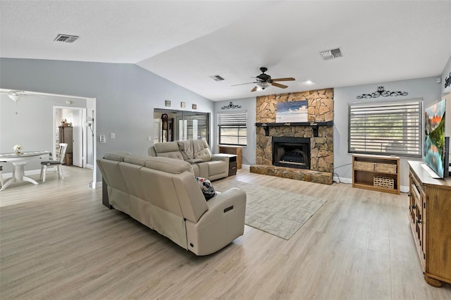 living area with vaulted ceiling, ceiling fan, a fireplace, and visible vents