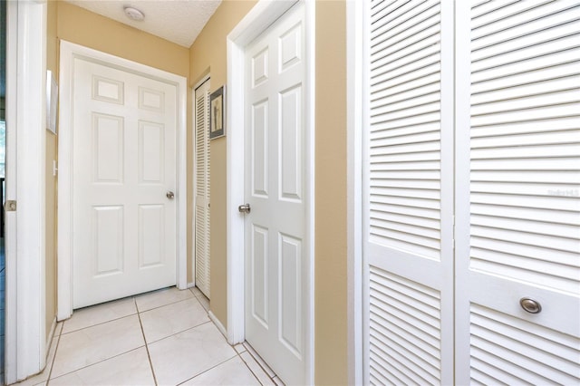 hallway with a textured ceiling and light tile patterned flooring