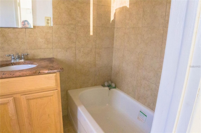 bathroom with vanity, a washtub, tile walls, and tasteful backsplash